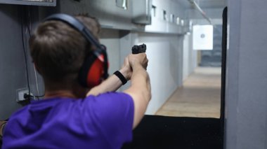 Shooter and instructor at shooting range. Man with gun and headphones shoots at target close up.