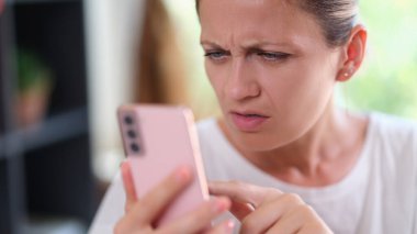 Woman with serious face looks doubtful at smartphone screen. Close-up of not confident woman with mobile phone.