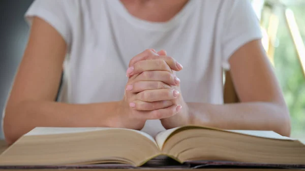 Woman reads thick book and prays close up. Connected female hands on open book. Religion, hope and learning concept.