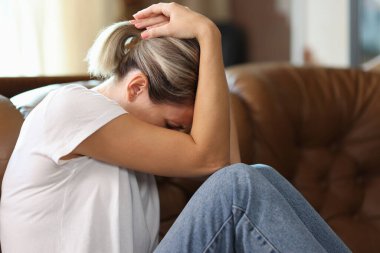 Sad exhausted woman holding her head with her hands while suffering on couch at home. Stress, health problems and loneliness concept.