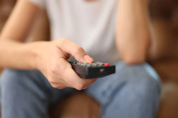 Woman holds remote control in her hand while sitting on sofa. Female hand with tv remote close up. Vacation at home, watching tv and television content concept.