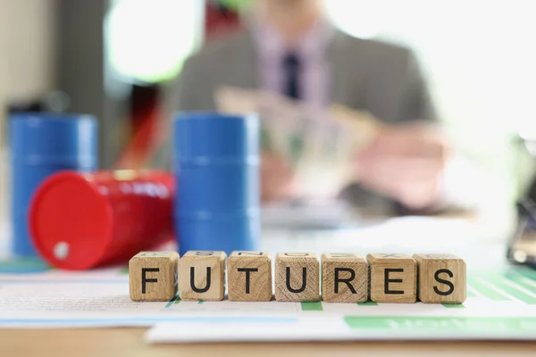 Oil futures and trading concept. Word futures collected from wooden cubes and oil barrels on financial statements, business man with money in background.