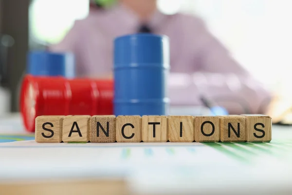 International sanctions and regulation of oil trading. Colorful oil drums on financial statements, letters sanction and blurred business man in background.