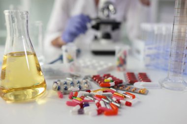 Tablets and yellow liquid in a flask on a table in the laboratory, close-up. Chemical analysis of medications