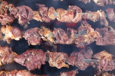 Top view of many metal skewers with meat in bbq grill. Grilling meat on open fire close up.