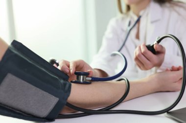 Doctor uses sphygmomanometer with stethoscope to check blood pressure of patient in hospital. Close up of blood pressure measuring, health care concept.
