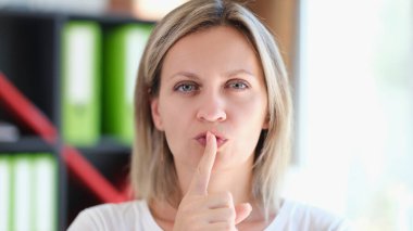 Adult woman holds finger on her lips and gestures to be silent and keep secret. Conspiracy, secrets and keep quiet concept.