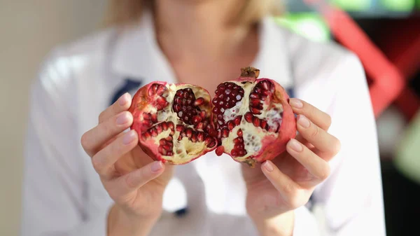 Female nutritionist show pomegranate as important source of vitamins, antioxidants and microelements. Close-up of doctor asks to eat healthy organic food to prevent diseases.