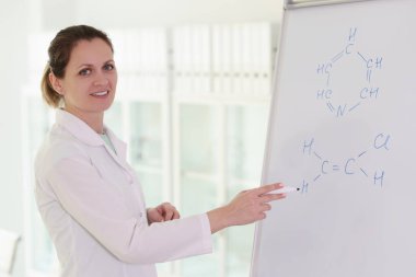 A smiling woman, a scientist writes a chemical formula on a white board, a close-up. Chemistry training, discovery