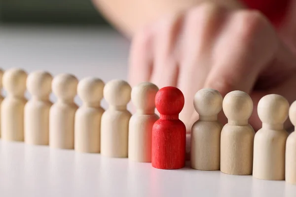 Red wooden figure in a number of white wooden figures in a row, close-up. Concept aggression in the team