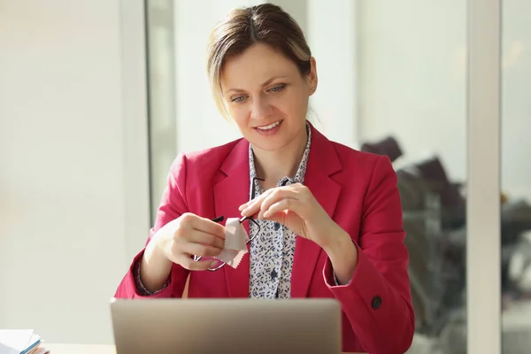 A happy woman in an office in front of a laptop wipes glasses, a close-up. Working video conference