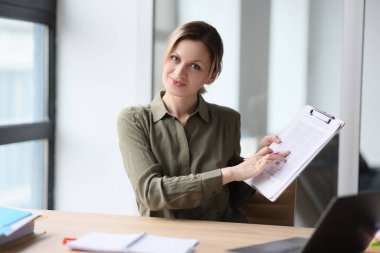 A beautiful woman at a table in the office shows documents, a close-up. Financial presentation