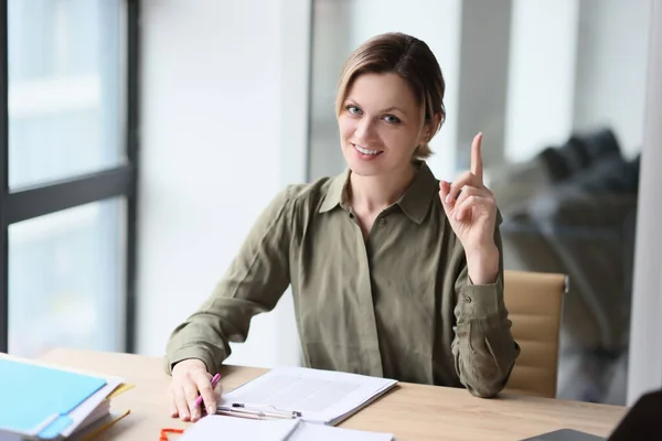 A smiling happy woman in the office shows the index finger up, a close-up. Concept idea, enthusiasm