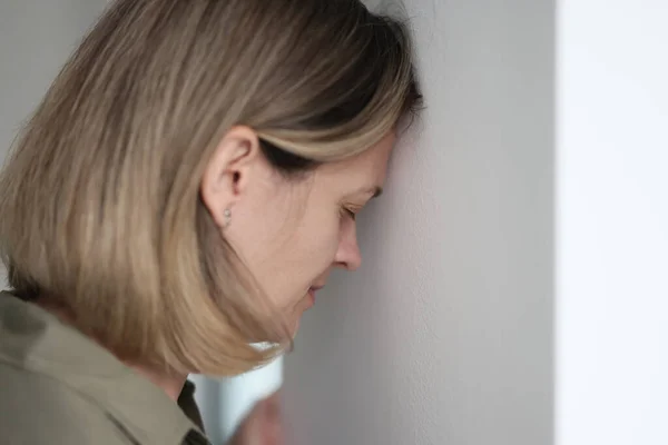 Sad young woman, leans against the white wall, closeup. Concept emotional burnout, mental pain