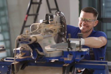A smiling worker serves a metal cutting machine, a close-up. Construction equipment, shallow focus