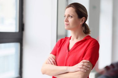 A young thoughtful woman in red clothes looks out the window, a close-up. Concept of thinking