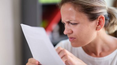 Daha net görebilmek için gözlerini kısarak metni okumaya çalışan odaklanmış bir kadının portresi. Görme sorunları nedeniyle metni görmekte zorlanan kadın