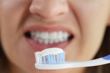 Close-up of woman holding tooth brush with snow white toothpaste, morning hygiene. Teeth cleaning and stomatology concept