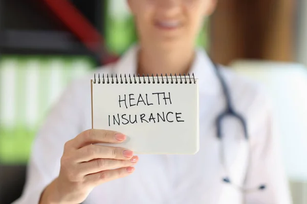 医療保険の言葉でメモ帳を示す女性医師のクローズアップ 健康労働者は健康保険を購入することを推奨する — ストック写真