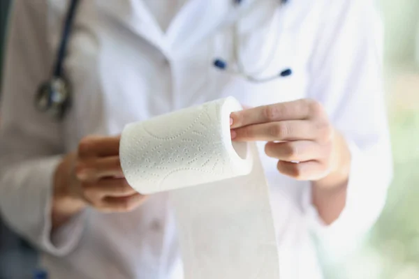 Close-up of female doctor holding toilet paper roll in hands. Paper roll for lavatory hygiene. Paper towel for hospital patients