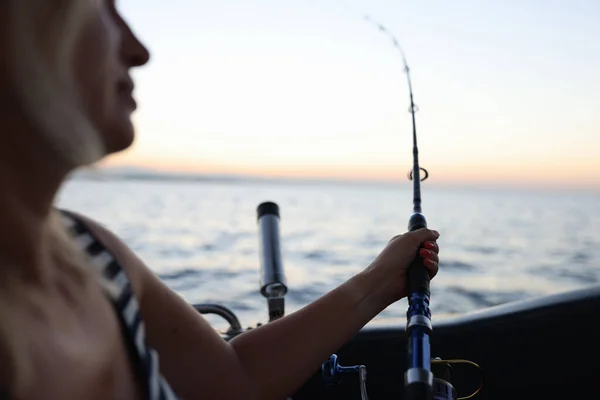 Woman is fishing on spinning rod in evening time. Sea fishing, tourism and hobby concept.