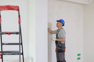 Kasklı tamirci evin duvarındaki sorunu kontrol ediyor. Ev onarımı ve yenileme konsepti.