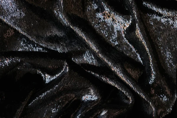 Wavy shining black fabric as background. Close up of black textile.