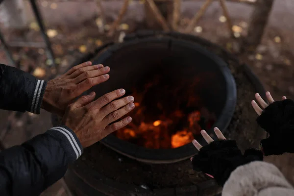 Female and male travelers warming their hands near bonfire. Cooking food on open fire and travel concept.