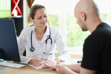 Kadın doktor, klinikteki hastasıyla konuşuyor. Terapist, hastane masasında otururken erkek hastaların teşhis ve tedavilerini açıklıyor..