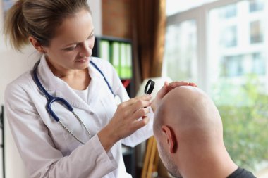 Doktor, klinikteki kel erkek hastanın kafa derisini kontrol ediyor. Saç restorasyonu ve dermatolojik hastalıklar kavramı.