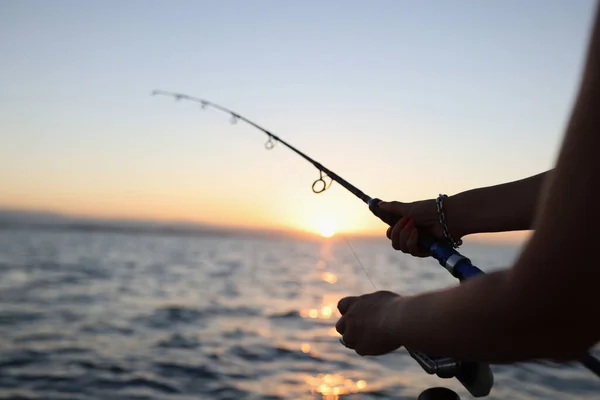 女性の手の中に釣竿を保持し 背景に海の上に夕日 観光客のための冒険の概念 — ストック写真