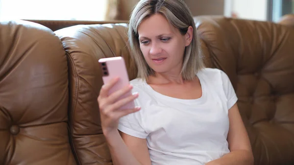 スマートフォンを持っているとソファに座っている間に画面を見て満足女性 オンラインコンセプトの売買とチャット — ストック写真