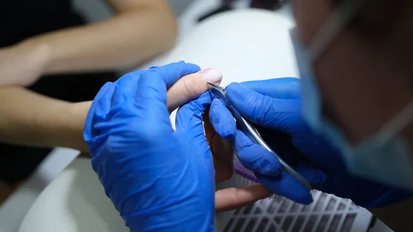 stock image Manicurist in latex gloves cuts cuticle of clients finger. Close-up of working beautician in spa salon.