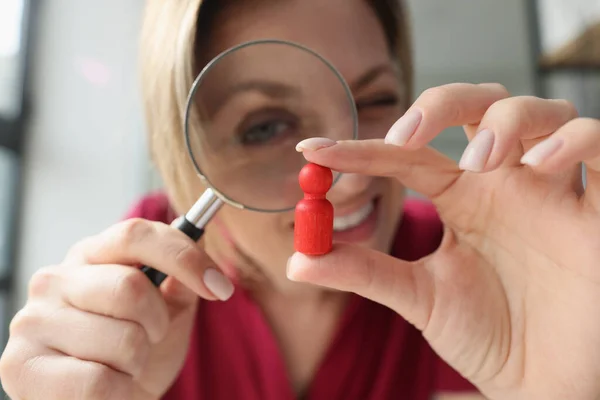 Business woman looking at red wooden figure through magnifying glass. Choosing personnel, hire employees and talents search concept.