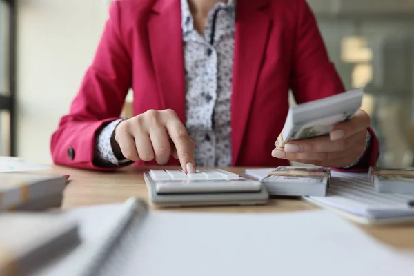 stock image Female accountant sits at her desk and counts money with calculator. Financial manager checks amount of cash on office desk.