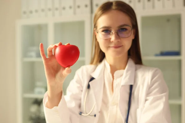 Young female cardiologist with stethoscope holds red heart in her hand. Concept of cardiology and heart health.