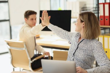 Kadın ve erkek modern ofiste masada otururken beşlik çakıyor. Mutlu meslektaşlar başarılı ortak projeyi tamamladı.