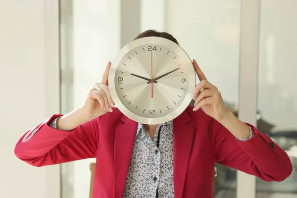 办公室里站着一个巨大的圆形挂钟 遮住了女人的脸 穿着红色夹克的员工用手握住时钟 工作时间管理 — 图库照片