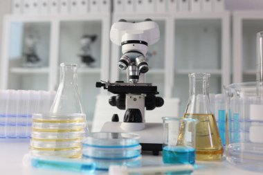 Sarı ve mavi sıvılı cam eşyalar masadaki modern mikroskoba karşı duruyor. Bilimsel araştırma için profesyonel laboratuvar ekipmanları