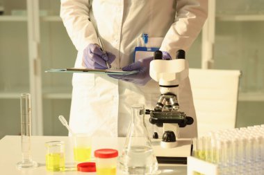Üniformalı kadın laboratuarda idrar testi yaptıktan sonra not alıyor. Profesyonel çalışan, masada duran verileri analiz ediyor