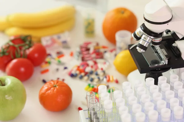 テーブルの上に顕微鏡やガラス管の近くに散在する丸薬に囲まれた新鮮な果物 研究室での薬や機器と有機食品 — ストック写真