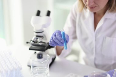 Kadın işçi mikroskop kullanarak test tüpünde numune inceler. Lastik eldivenli bir kadın labaratuvarda bilimsel araştırmalar yapıyor.