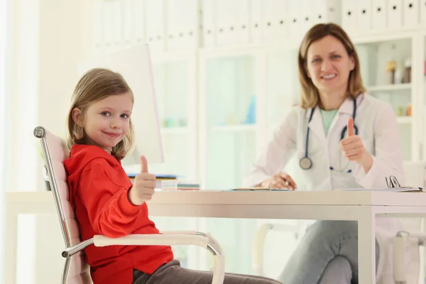 診療所の予約で女の子と医者が親指を立てている 小児科医の診察室 子どもの健康支援 — ストック写真