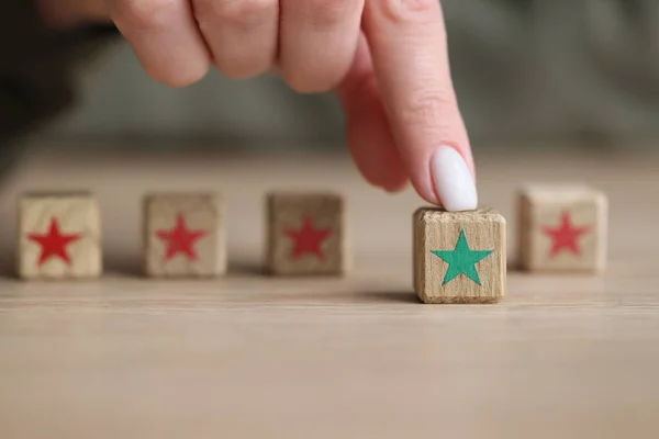 Finger of woman touches kids wooden cube with green star against blocks with red stars. Concept of leadership and nonconformity closeup