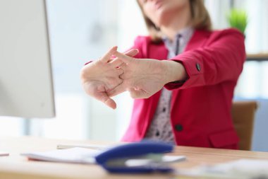 Kadın çalışan bilgisayarda çalışmaya başlamadan önce parmaklarını yoğurur. Kırmızı ceketli genç kadın teneffüste hafif ofiste masada oturuyor.