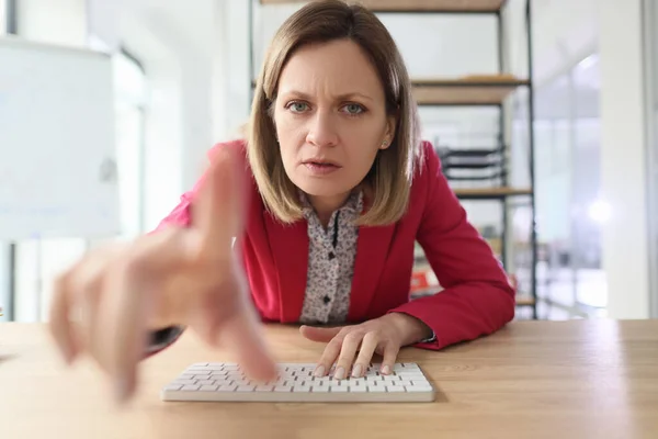 怒っている女性はキーボードを入力するモニターでインデックス指をポンと押します 疑わしいブロンドの女性労働者はウェブサイトの閉鎖上の小さなテキストを読もうとします — ストック写真