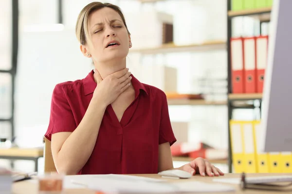 女はオフィスの密室の机に座って痛みを伴う喉に触れる 風邪の症状を持つ従業員 ウイルス感染症の危険性 — ストック写真