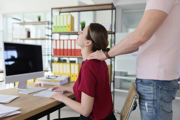 Colleague does neck massage to woman at workplace in company office closeup. Male coworker helps friend to relax. Tension and stress reducing
