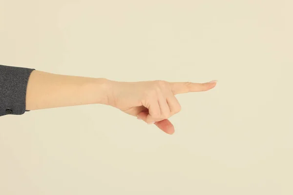 Hand of woman pointing index finger on beige background. Female person shows pointing gesture to make notice of certain object closeup