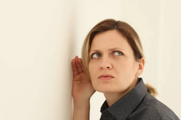 Concentrated woman listens to discussion of friends in kitchen. Attentive female person puts ear close to wall to hear and find out secrets closeup